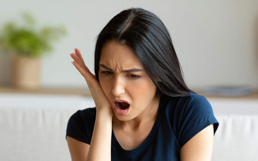 woman wearing a navy tank top holding the side of her mouth in dental pain