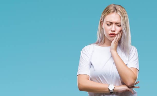 Blonde girl holding the side of her face in pain from toothache on a blue background