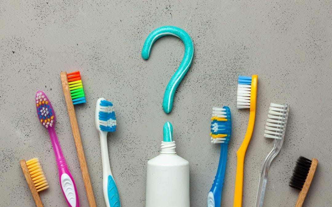 Toothpaste in the form of a question mark and many different and colored toothbrushes. Concept of how to choose the right toothbrush or how to brush your teeth.
